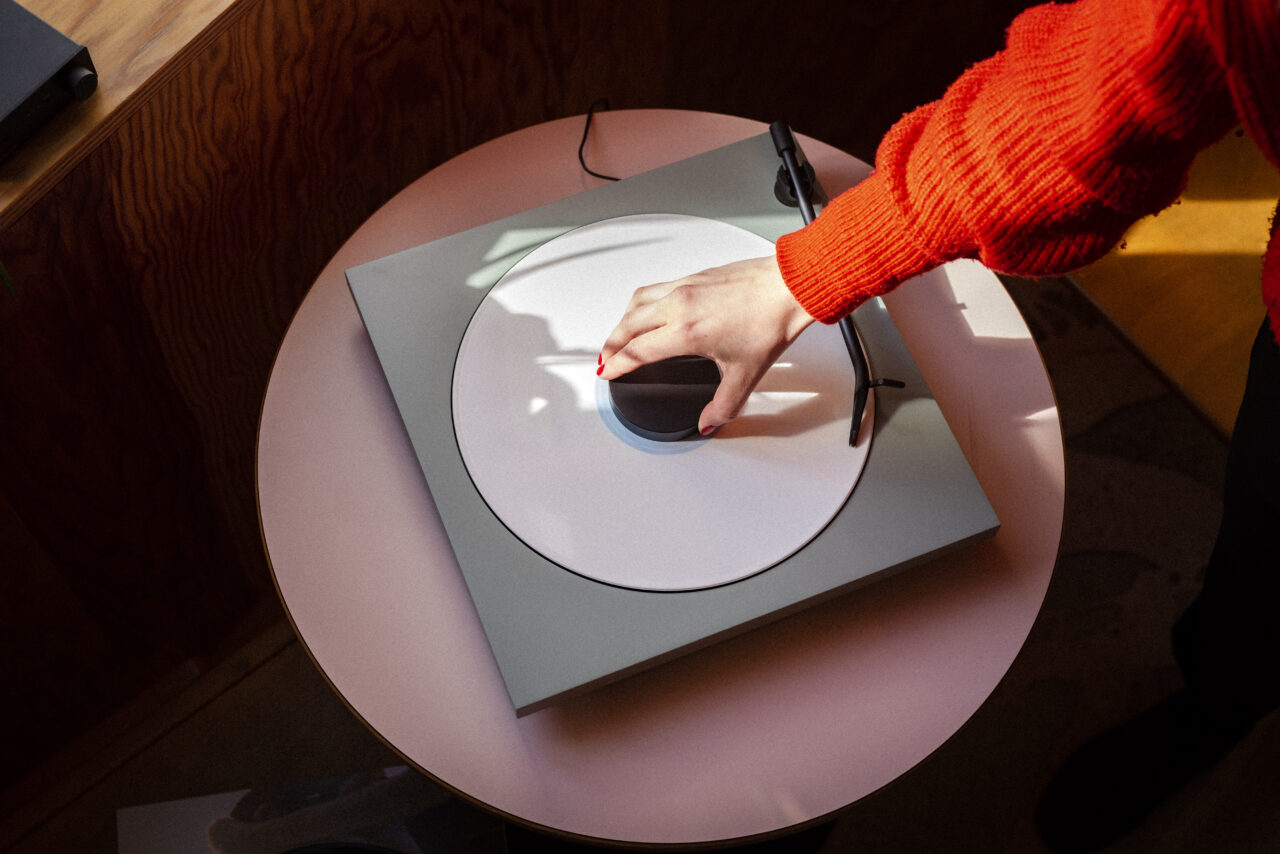 Tone turntable, satin green, tone puck, white vinyl record, pink table, red pullover, woman hand